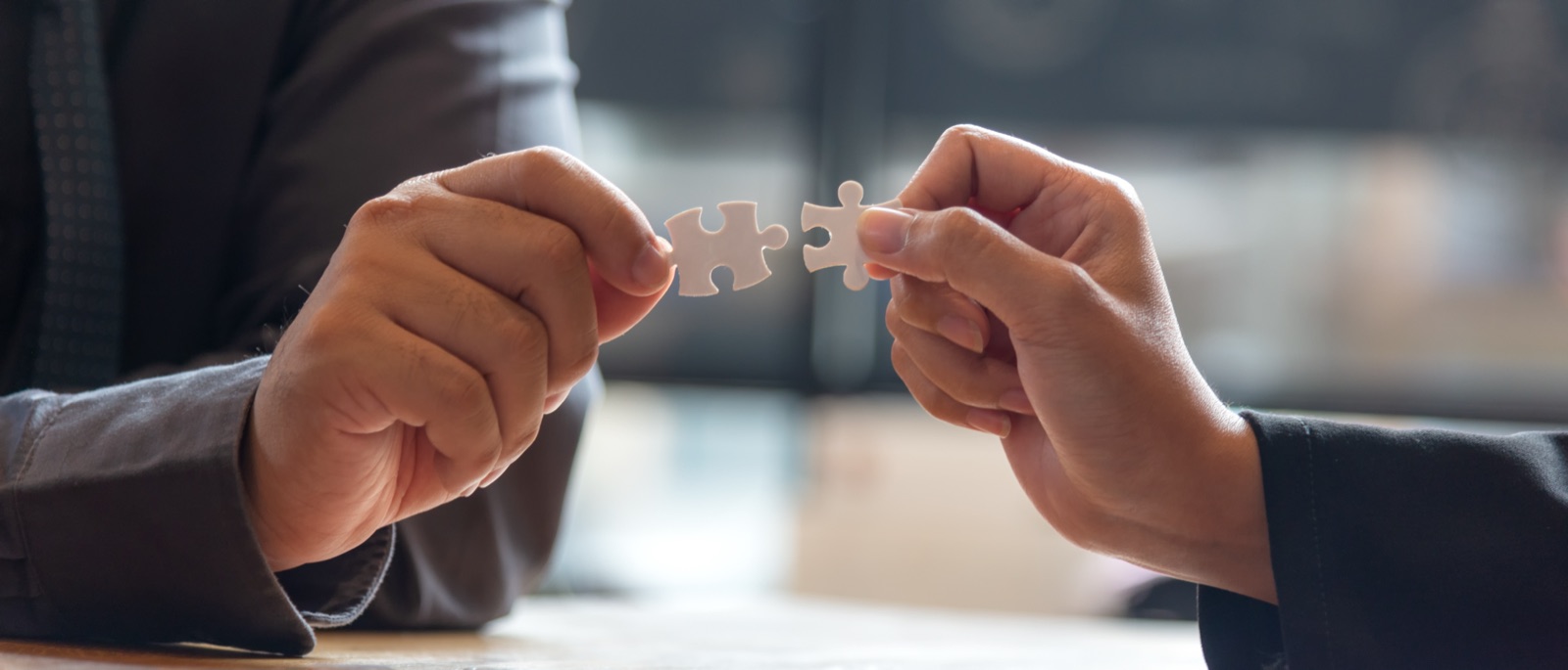 Two people connecting jigsaw puzzle pieces across a desk